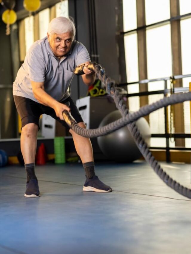 Active senior men in sportswear training with battle rope in gym gym